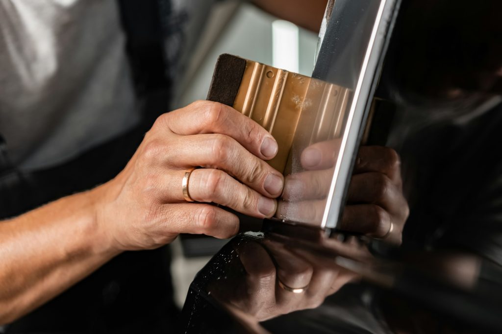 Worker applies car protection film on a car in detailing service